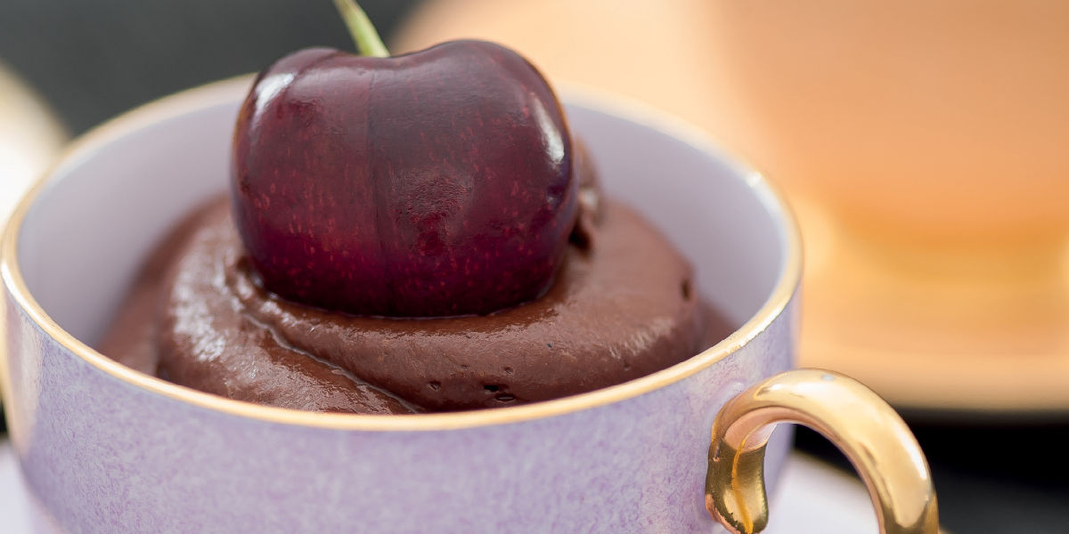 Portion of chocolate mousse in a cup with a cherry on top